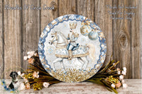A decorative plate featuring a man in a blue and gold outfit riding a white horse, surrounded by a wreath of flowers and greenery.