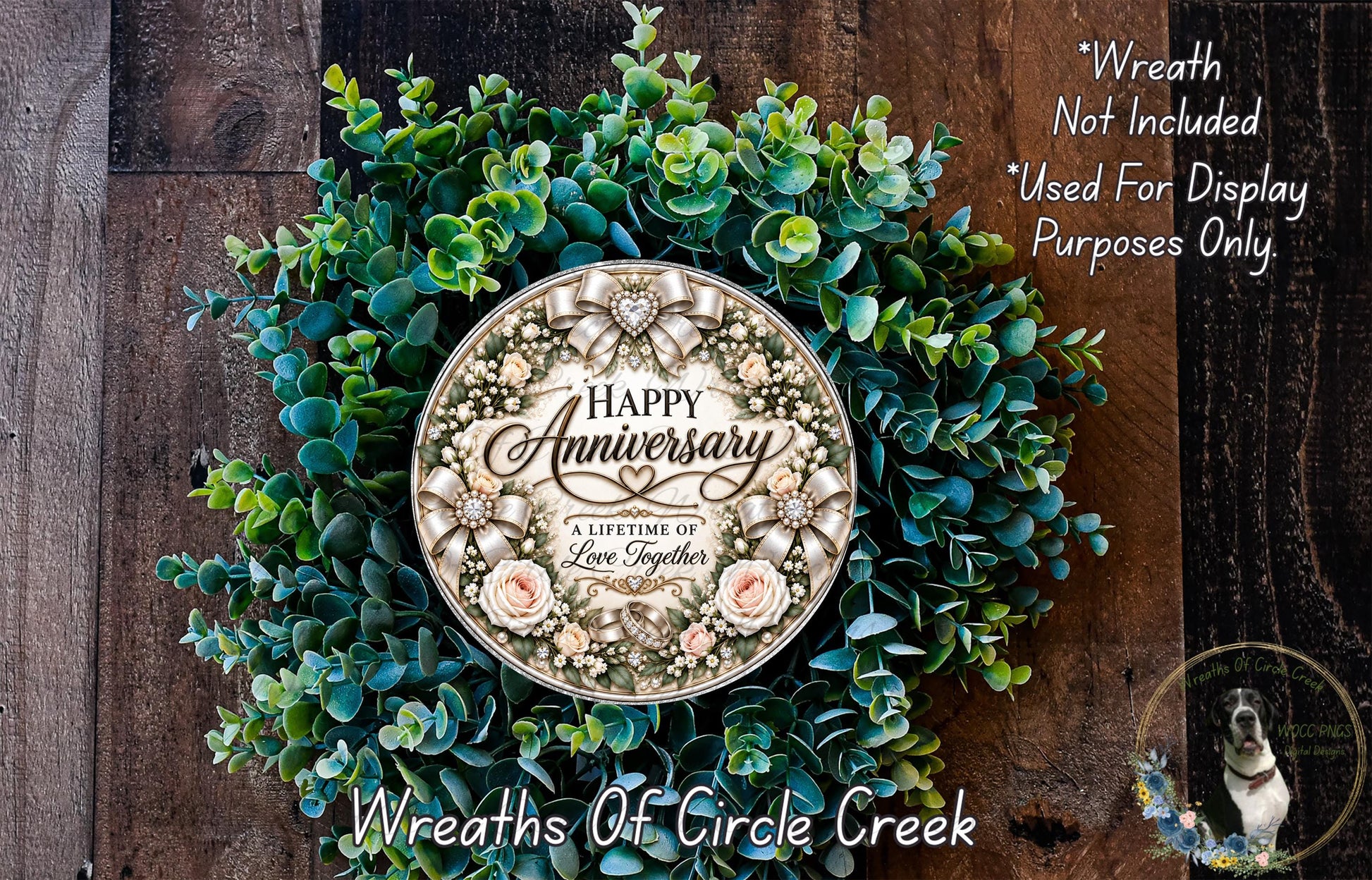 a wreath made of green leaves and flowers, with a large circular plaque in the center that reads "Happy Anniversary" and "A Lifetime of Love Together". The wreath is displayed on a wooden surface, and there is a small dog in the bottom right corner of the image.