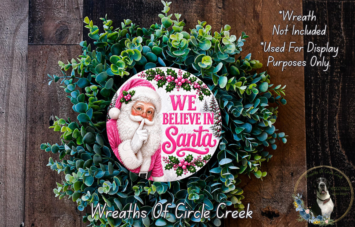 A wreath made of green leaves and flowers, featuring a Santa Claus image and the text "We Believe in Santa" in pink and white.