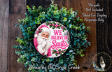 A wreath made of green leaves and flowers, featuring a Santa Claus image and the text "We Believe in Santa" in pink and white.