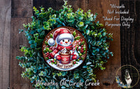 A wreath made of green foliage and featuring a snowman wearing a red hat and scarf, holding a cup of hot cocoa.