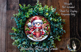 A wreath made of green foliage and featuring a snowman wearing a red hat and scarf, holding a cup of hot cocoa.