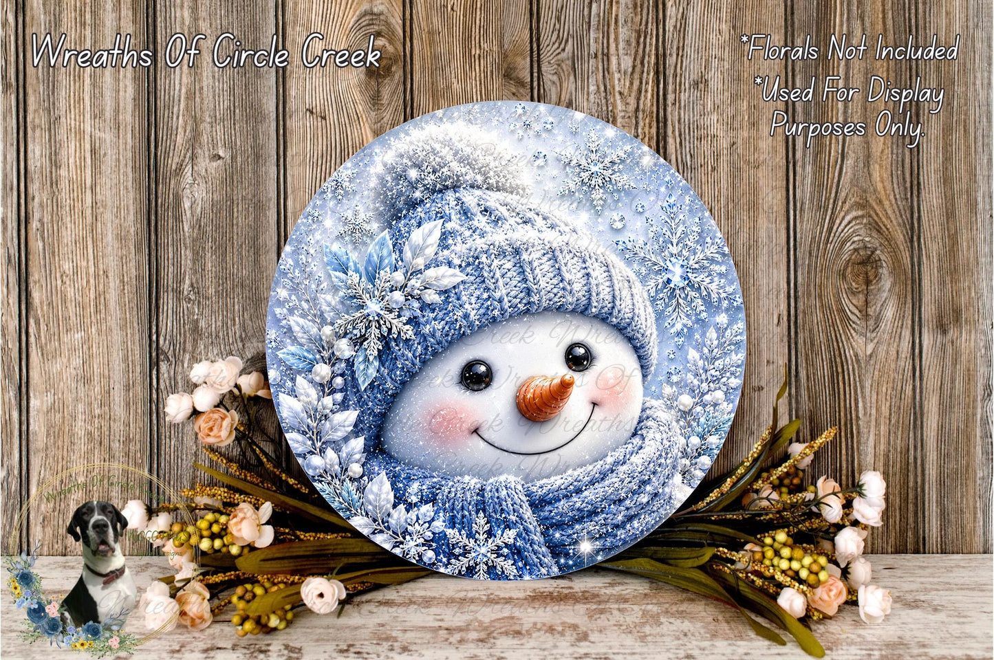A snowman decoration with a blue scarf and hat, surrounded by flowers and placed on a wooden surface.