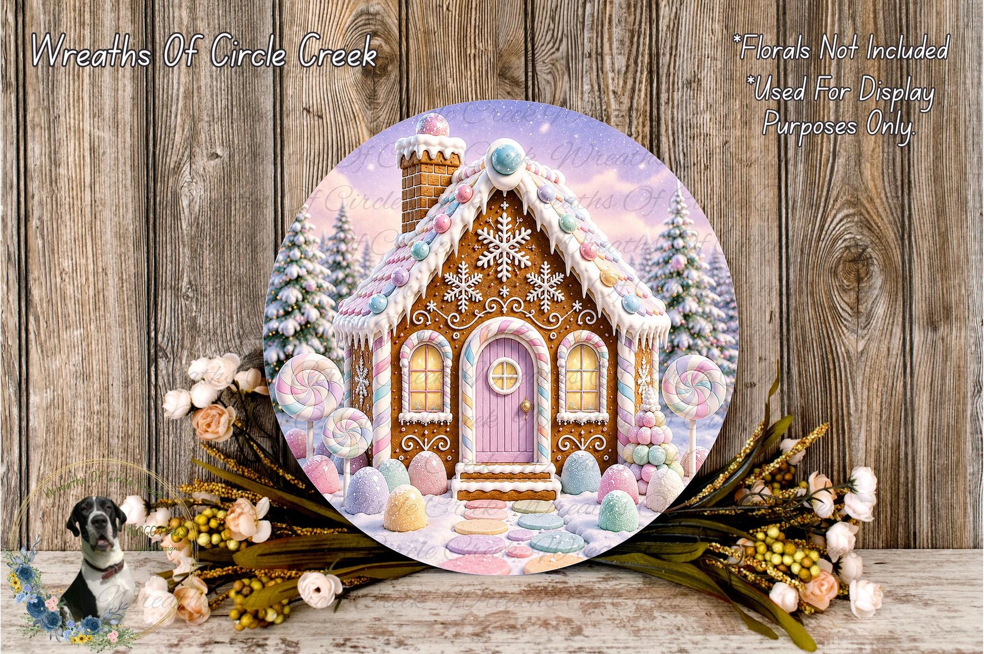 A round, decorative wreath featuring a whimsical gingerbread house with a snow-covered roof, surrounded by flowers and greenery.