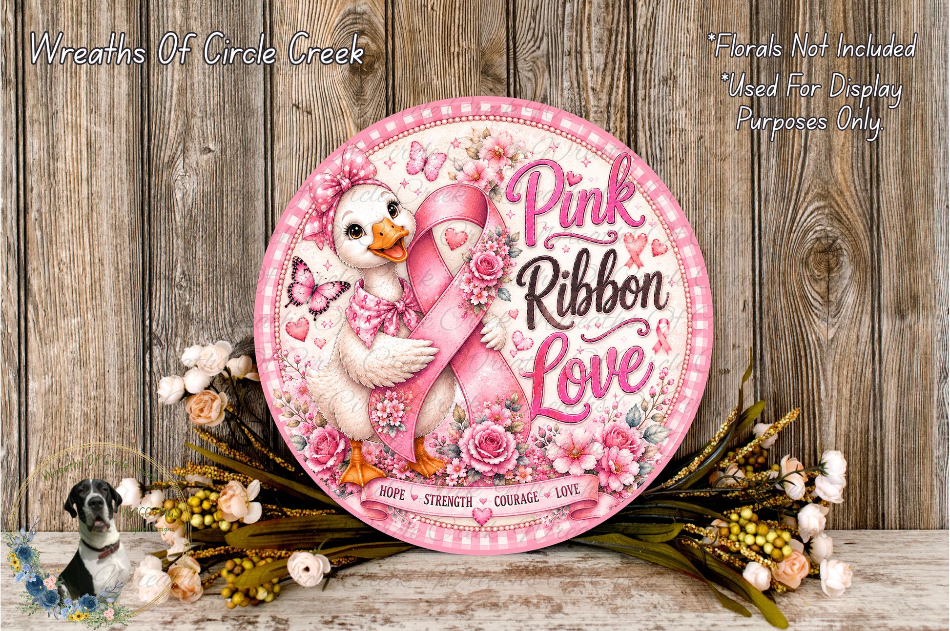 A decorative sign featuring a pink ribbon and a duck holding a pink ribbon, surrounded by flowers and placed on a wooden surface.