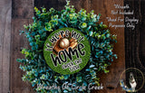 The image is a wreath made of various green plants and a baseball glove, with the text "If we were not home, we would check the field" displayed on it.