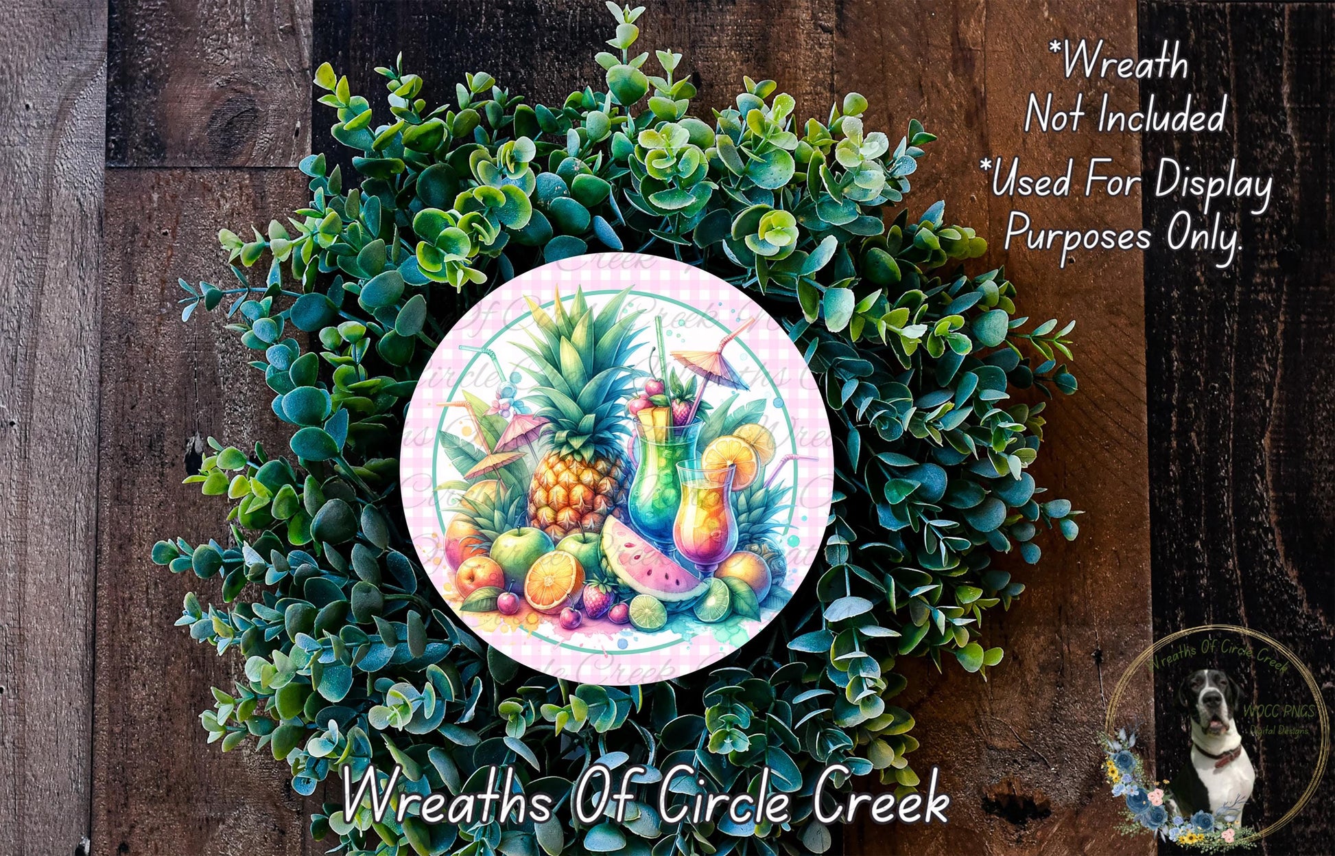 A wreath made of various green plants and fruits, including pineapple, watermelon, and oranges, is displayed on a wooden surface.