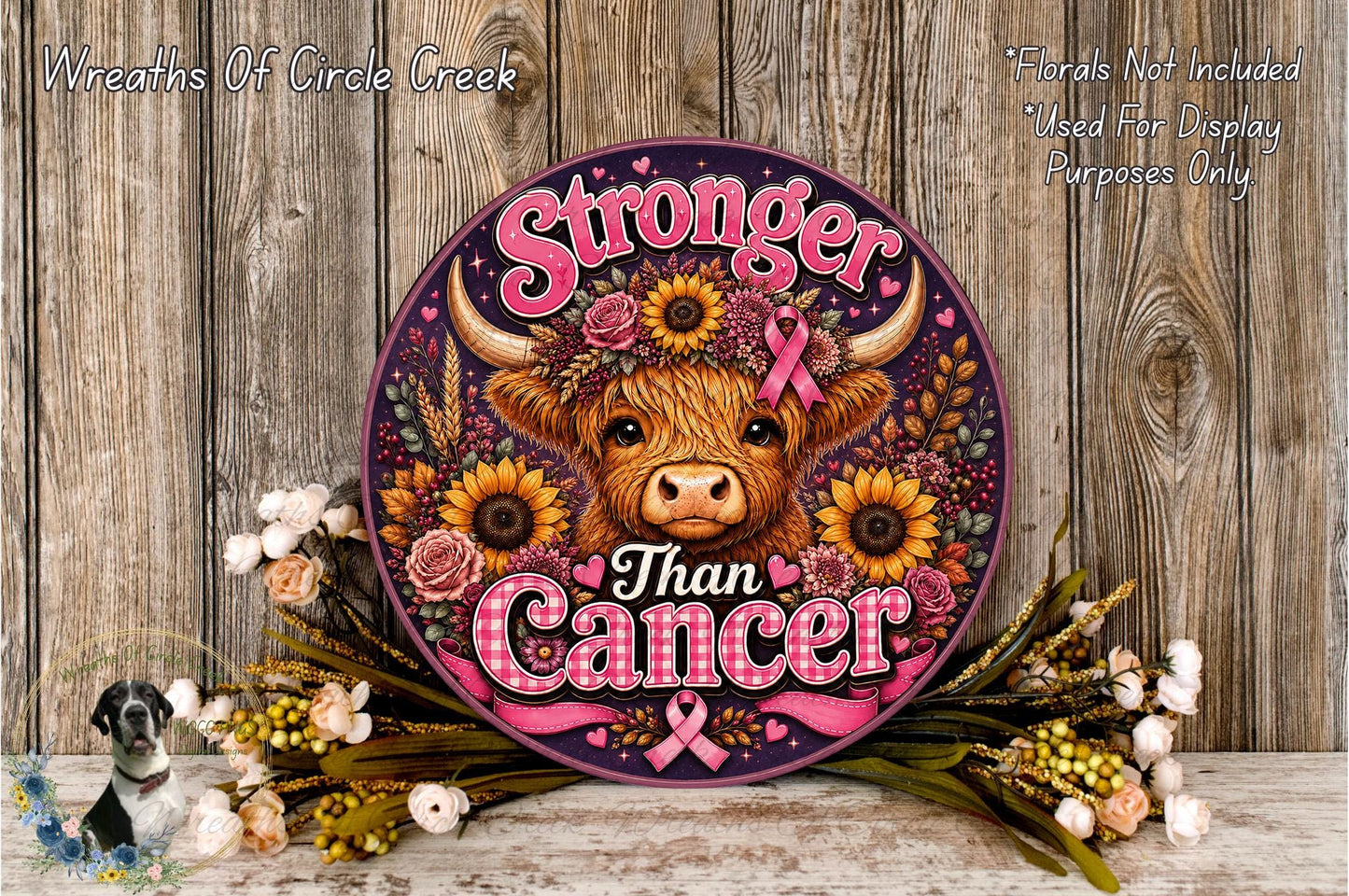 a round sign with a cow's head and floral elements, surrounded by flowers and placed on a wooden surface.