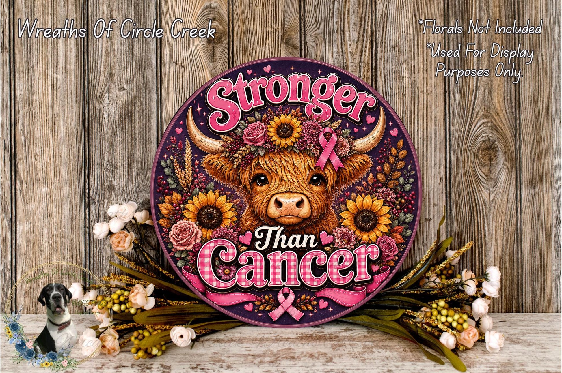 a round sign with a cow's head and floral elements, surrounded by flowers and placed on a wooden surface.