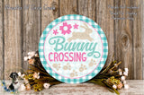 a round sign with the text "Bunny Crossing" and a decorative border, surrounded by a floral arrangement and a wooden background.