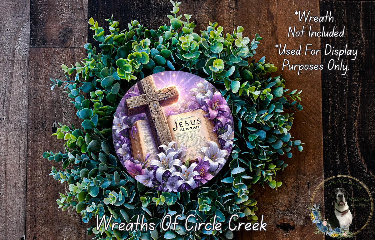 A wreath made of green and purple flowers, with a wooden cross and a book titled "Jesus" displayed on it.