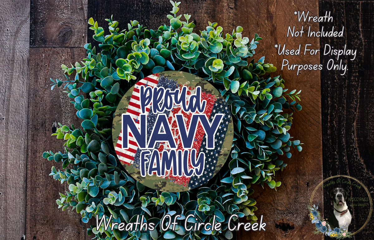 a wreath made of green leaves and a circular sign with the text "Proud Navy Family" in the center. The wreath is displayed on a wooden surface, and there is a small dog in the bottom right corner of the image.