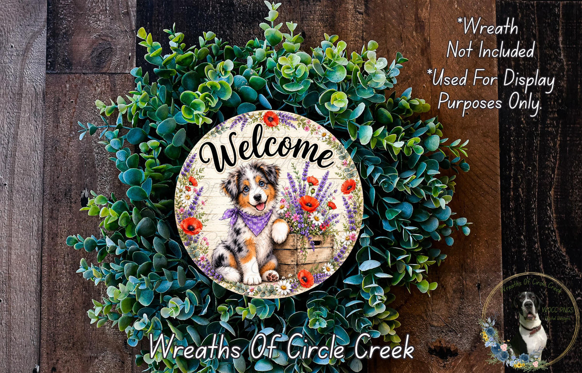 a wreath with a dog sitting in a basket, surrounded by green leaves and flowers. The wreath is displayed on a wooden surface, and there is text that reads "Welcome Wreath Not Included * Used For Display Only. Purposes Only."