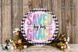 a decorative sign with the text "SAVED BY HIS GRACE" in a colorful, artistic style. The sign is surrounded by a wreath of flowers and placed on a wooden surface.