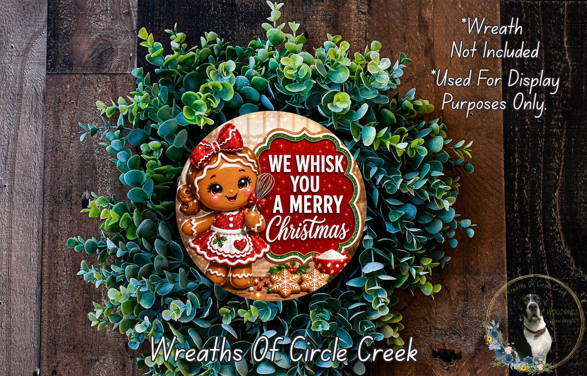 A wreath made of green foliage and featuring a gingerbread girl with a red bow, surrounded by the text "We Whisk You A Merry Christmas".