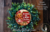 A wreath made of green foliage and featuring a gingerbread girl with a red bow, surrounded by the text "We Whisk You A Merry Christmas".
