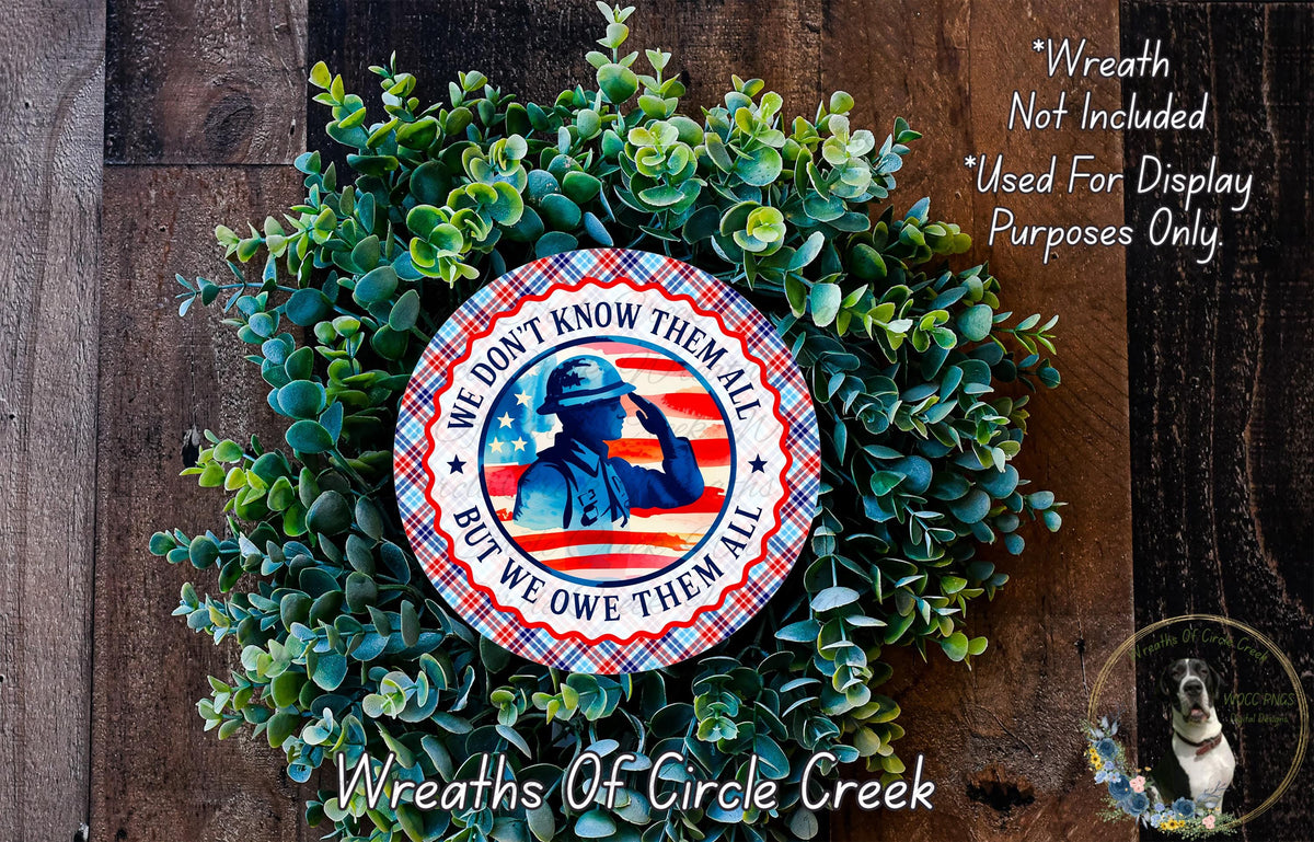 A wreath made of green leaves and a circular patriotic design featuring a firefighter silhouette and the text "We don't know them all but we owed them all".