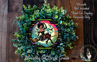 A wreath made of green plants and featuring a woman dressed as a witch, with a colorful and whimsical design.
