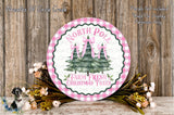 a round sign with a Christmas tree design, surrounded by flowers and placed on a wooden surface.