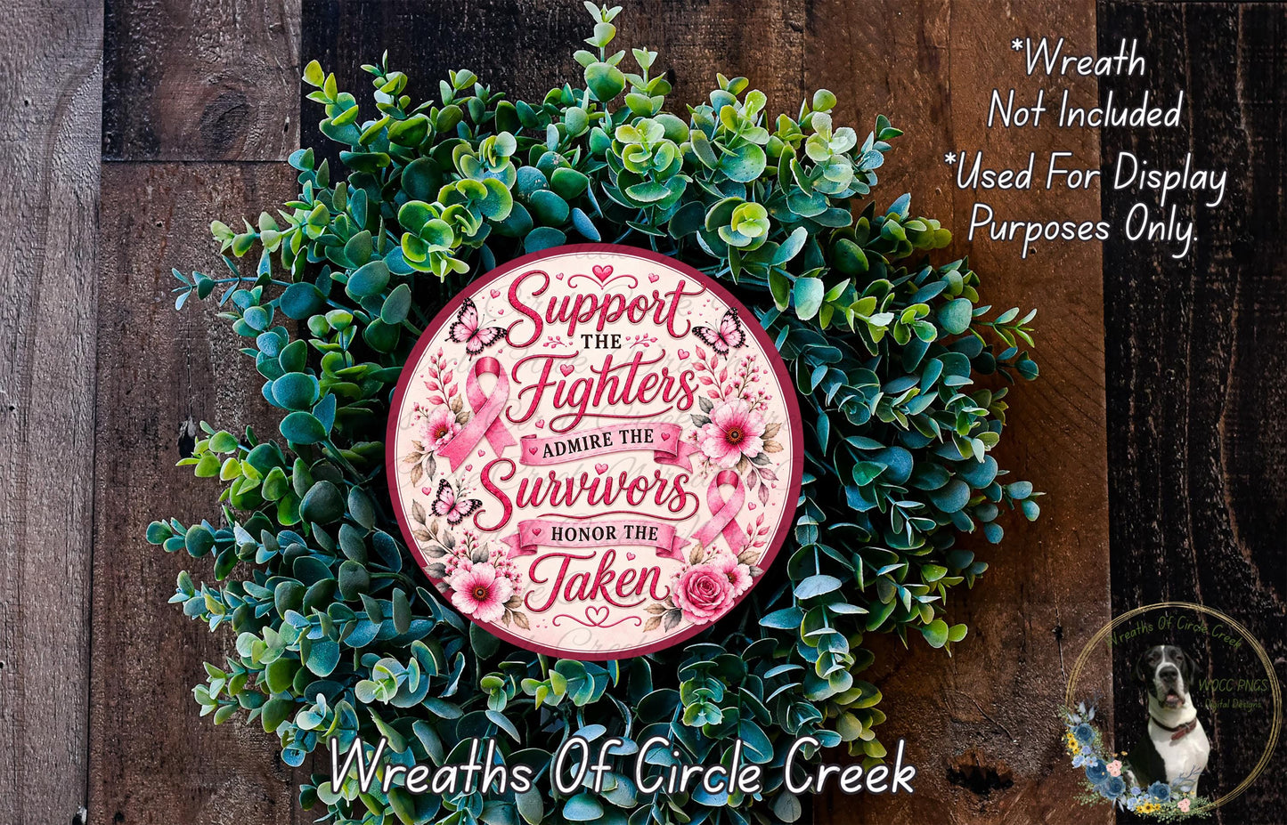 a wreath made of green leaves and flowers, with a pink circular sign in the center that reads "Support the fighters, admire the survivors, honor the taken". The sign is surrounded by the wreath, and there is a small dog visible in the bottom right corner of the image.