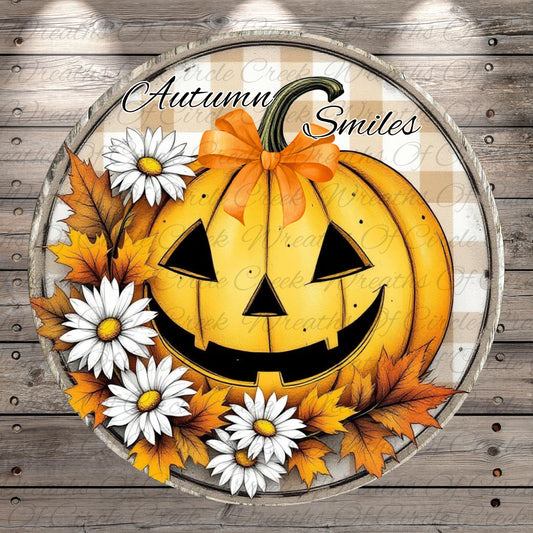 A Halloween-themed pumpkin decoration with a bow, surrounded by white daisies and autumn leaves, with the text "Autumn Smiles" written on the pumpkin.
