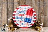 a round sign with a patriotic design, surrounded by flowers and a wooden background.