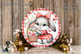A round, decorative plate featuring a cartoon rabbit wearing a red and white checkered dress and holding a basket of Easter eggs, surrounded by flowers and a wooden background.