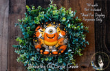 A wreath made of green leaves and featuring a large, colorful monster with a yellow eye and orange and black striped body.