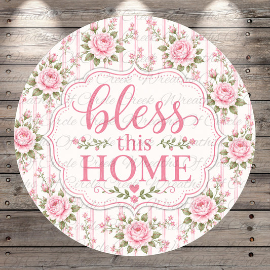 A round floral sign with the text "bless this home" in a decorative font, surrounded by pink roses and greenery.