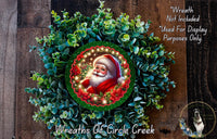 A wreath with a Santa Claus image in the center, surrounded by greenery. The wreath is displayed on a wooden surface.