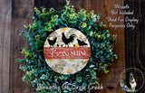 a wreath made of green foliage and a circular sign with the text "Rise & Shine" and a rooster silhouette. The sign is surrounded by a lush wreath, creating a decorative and festive display.