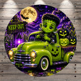 A green vintage truck with a carved jack-o-lantern on the back, driving down a road with a full moon and bats in the background. The truck is labeled "MONSTER" and there is a "KEEP OUT" sign visible.