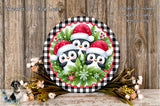 A festive Christmas wreath with three cheerful penguins wearing Santa hats, surrounded by greenery and flowers, displayed on a wooden surface.