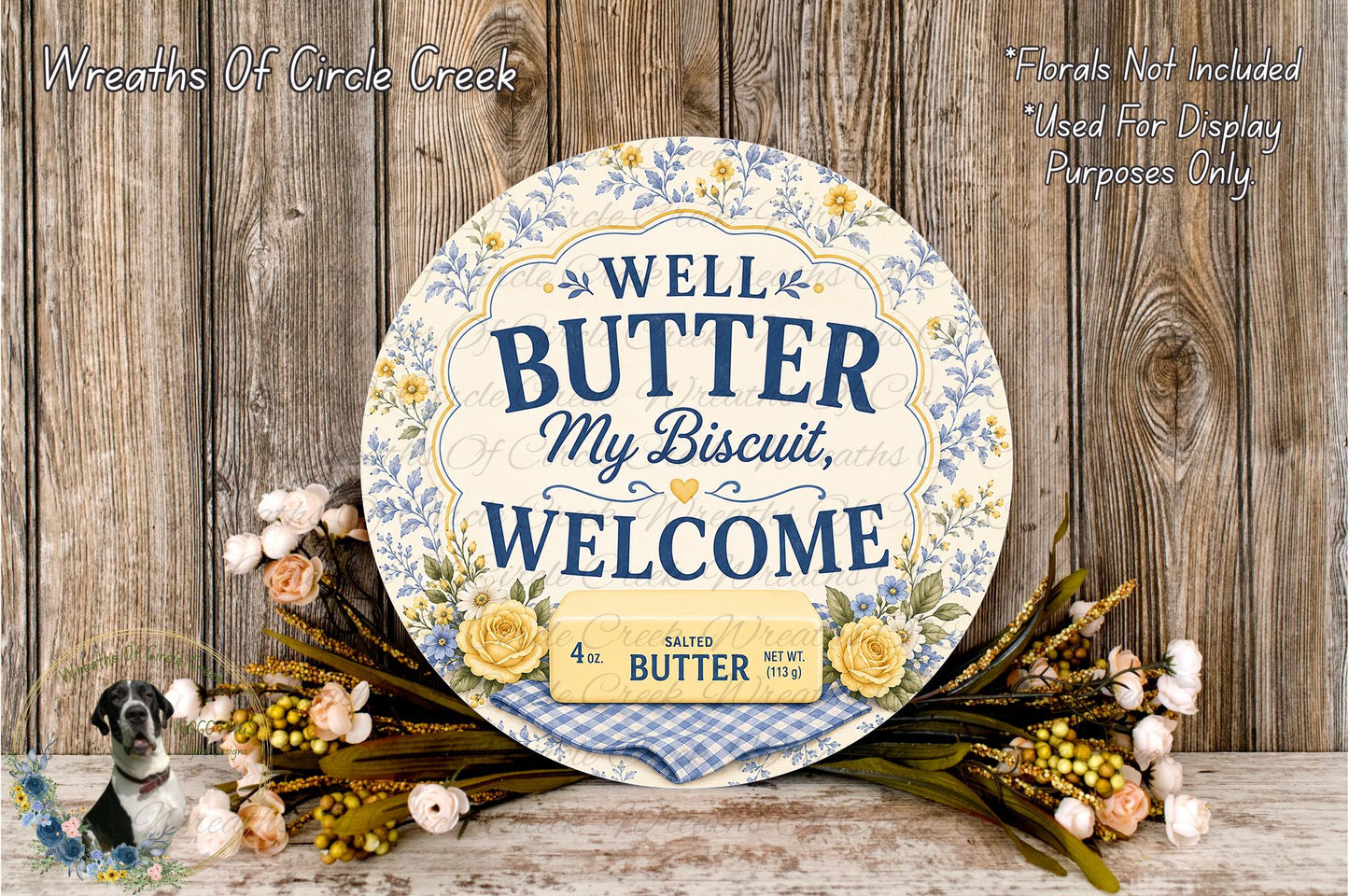 a decorative sign with the text "WELL BUTTER MY BISCuit, WELCOME" and a weight of 4.5 oz. The sign is surrounded by a floral arrangement and placed on a wooden surface.