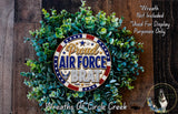 a wreath made of green leaves and a circular emblem with the text "Proud Air Force Brat" on it, placed on a wooden surface.