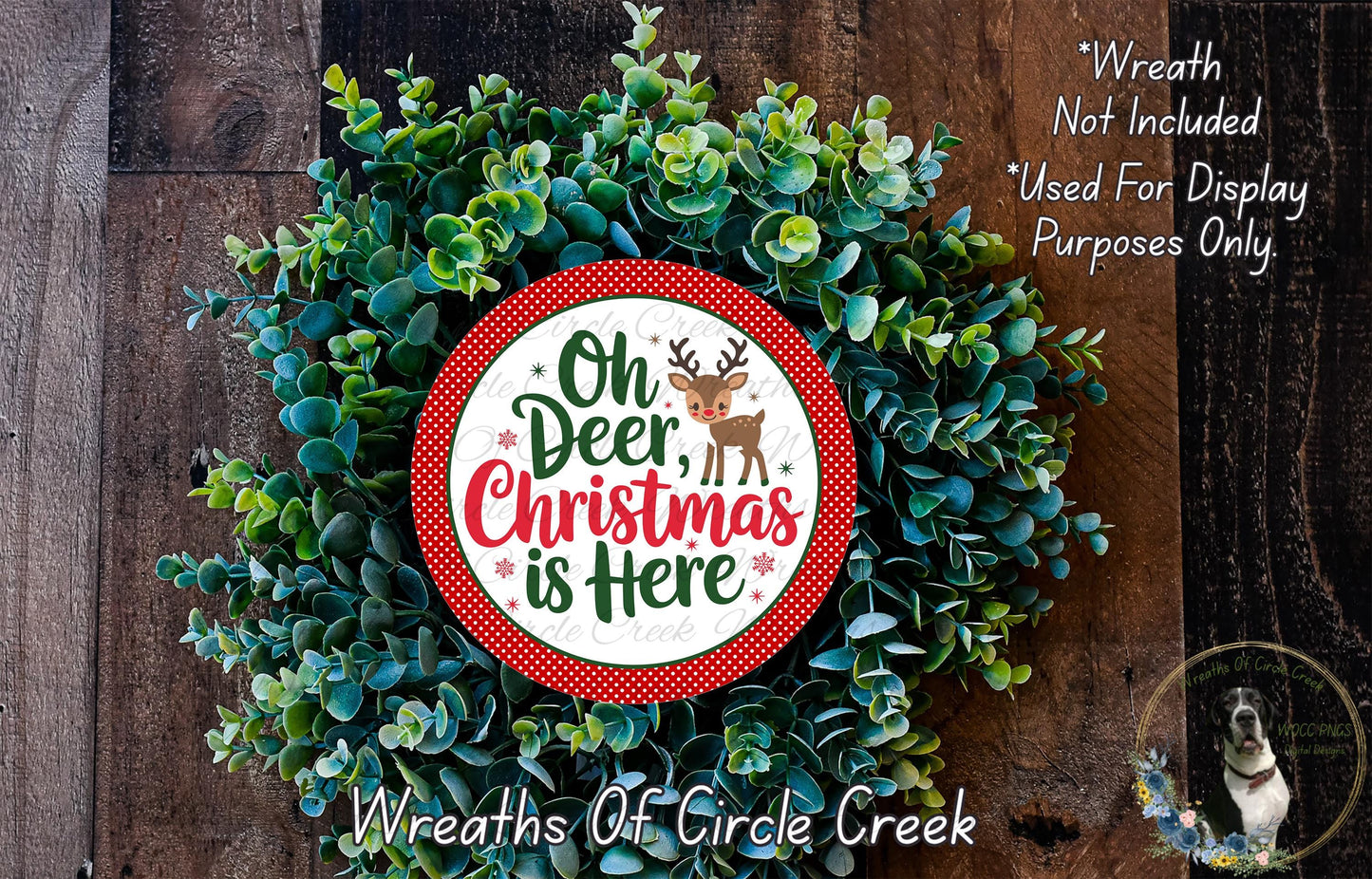 A Christmas wreath made of green leaves and a red and white circular sign that says "Oh Deer, Christmas is Here".