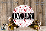 a round sign with the word "LOVE SHACK" written on it, surrounded by a floral arrangement and a wooden background.